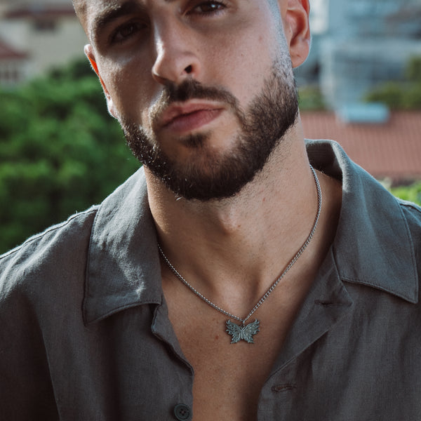 Mand bærer sølvfarvet halskæde med sommerfugl-vedhæng