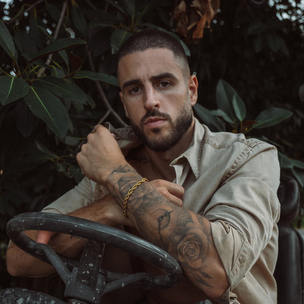 Mand med guldbelagt armbånd og tatoveringer i beige skjorte