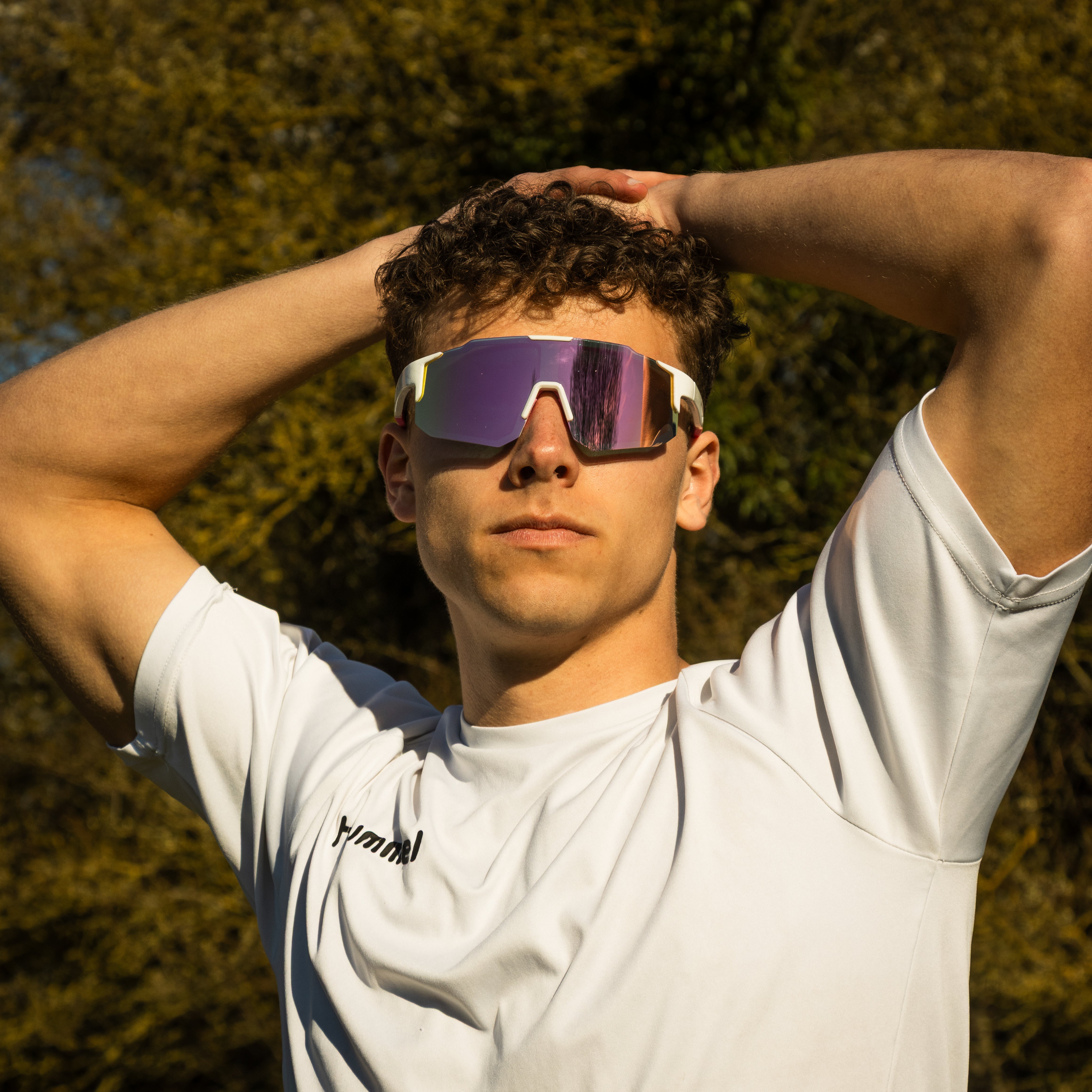 Mand i hvid trøje bærer Noire Glamour sportsbriller med lyserøde spejlglas udendørs