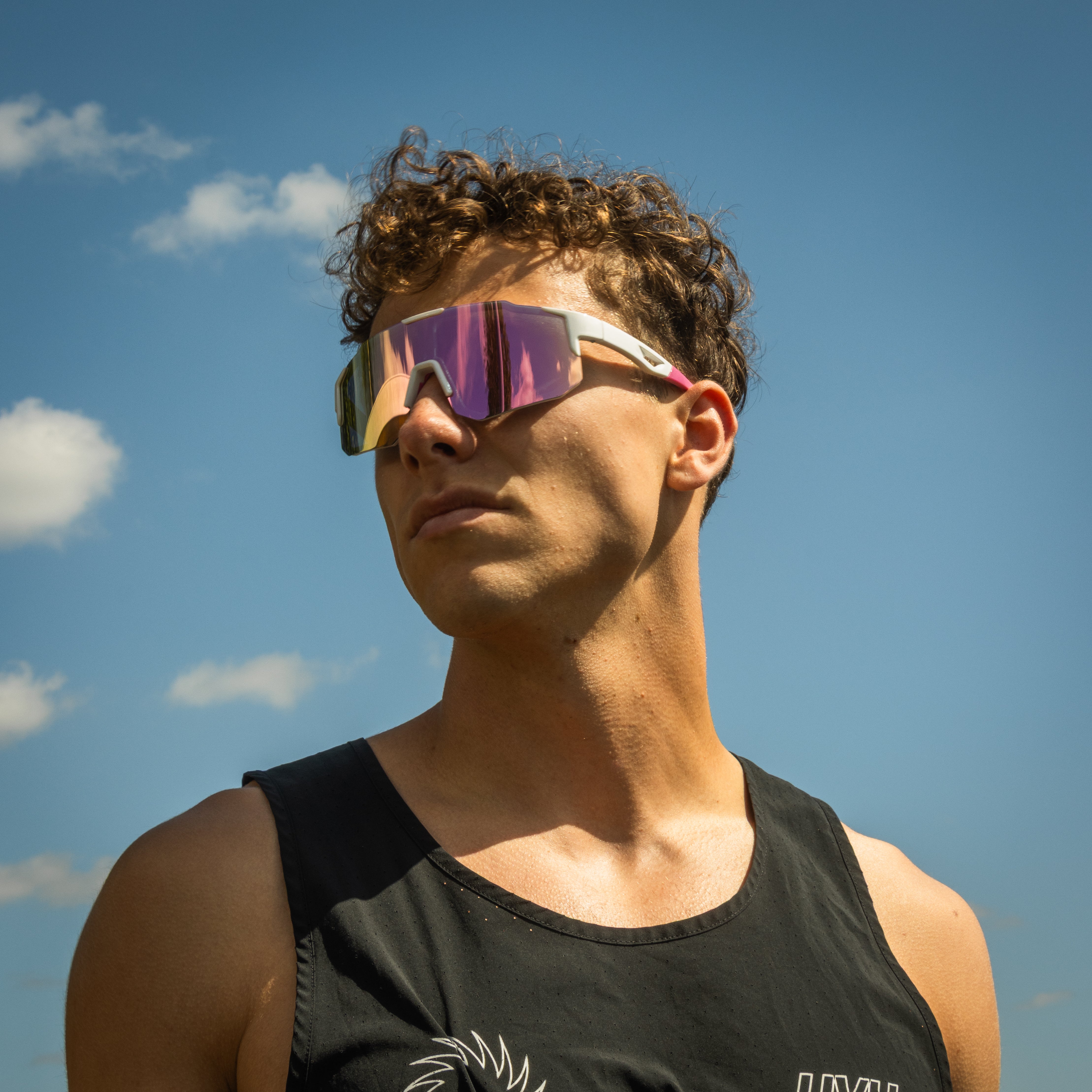 Mand bærer Noire Glamour sportsbriller i lyserød med spejlglas under blå himmel