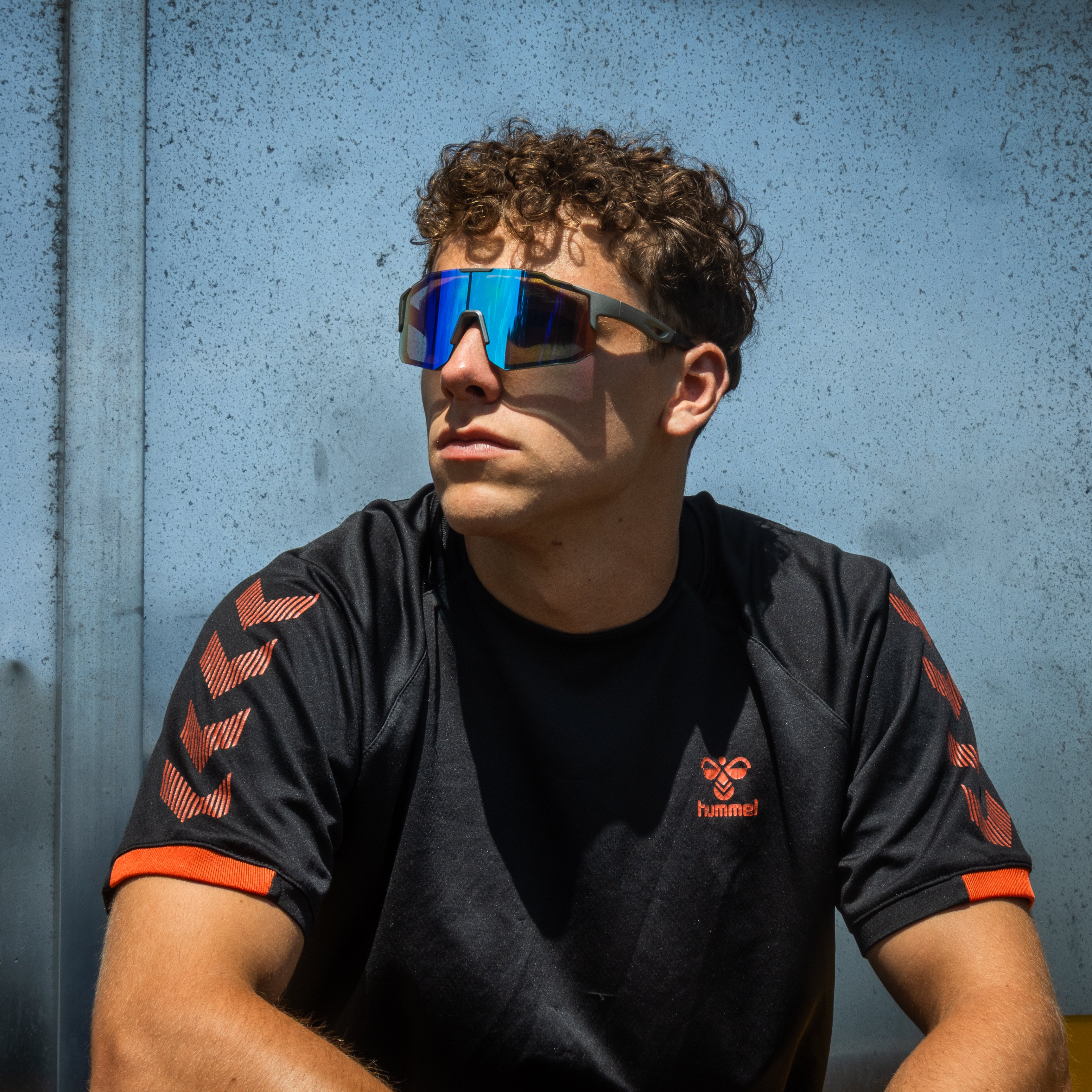 Mand bærer Noire Leafy sportsbriller med blå spejlglas foran lyseblå væg