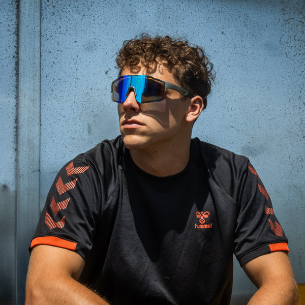 Mand bærer Noire Leafy sportsbriller med blå spejlglas foran lyseblå væg