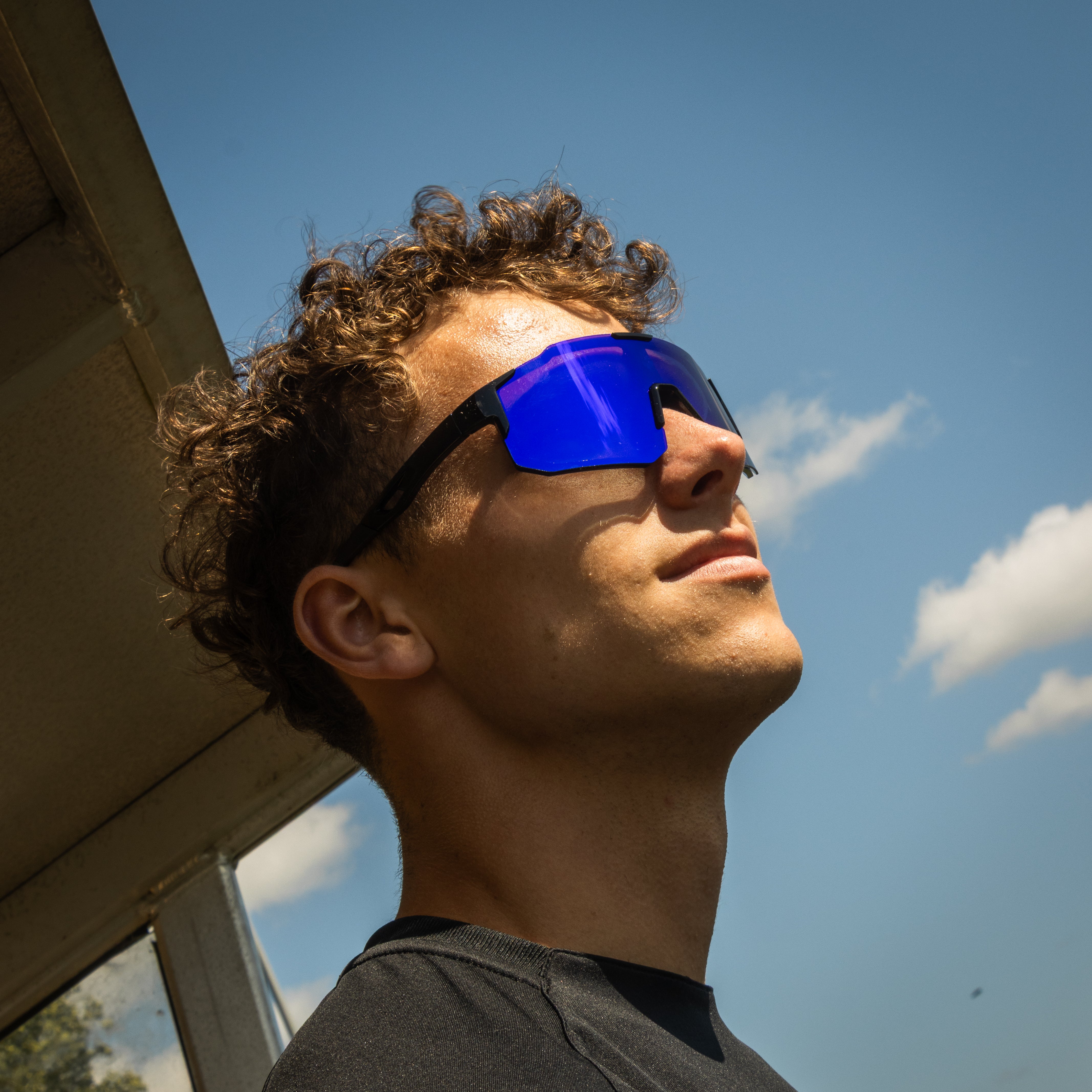 Sportsbriller med blå spejlglas på model set fra siden mod blå himmel