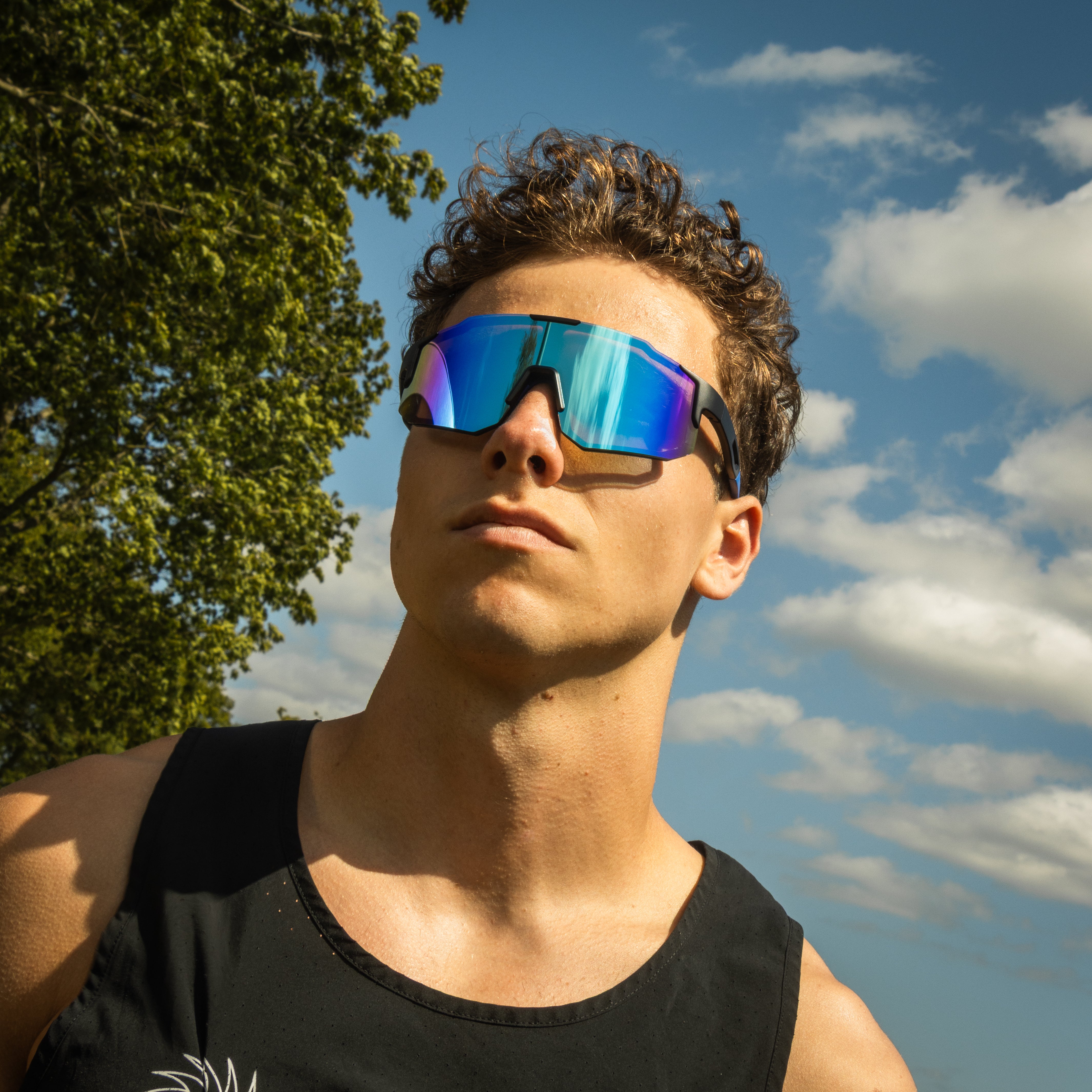 Mand bærer Noire Purplish sportsbriller med blå spejlglas udendørs i sollys