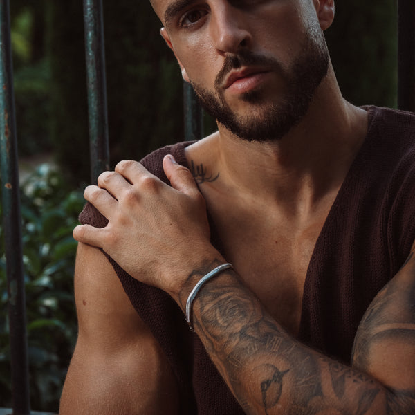 Mand med sølvfarvet armbånd og tatoveringer