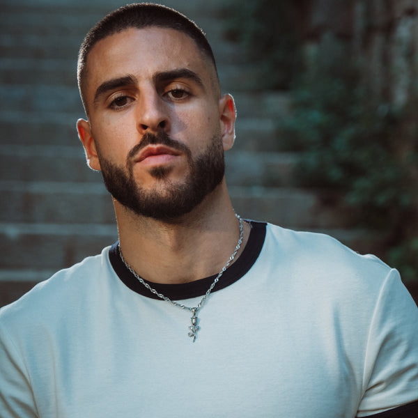 Mand med sølvfarvet rose halskæde og lyseblå t-shirt