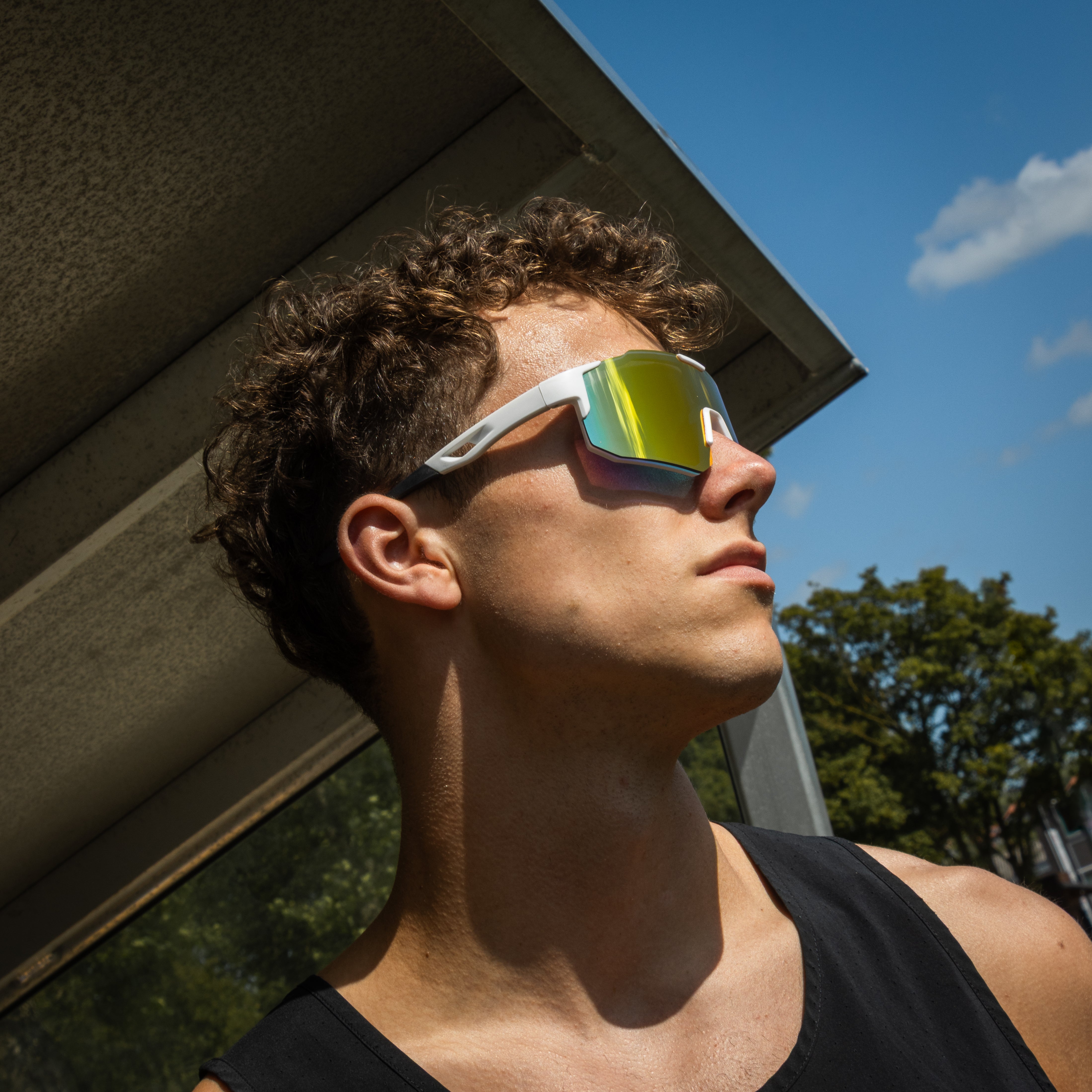 Sportsbriller med hvid stel og spejlglas på model i profilvinkel udendørs