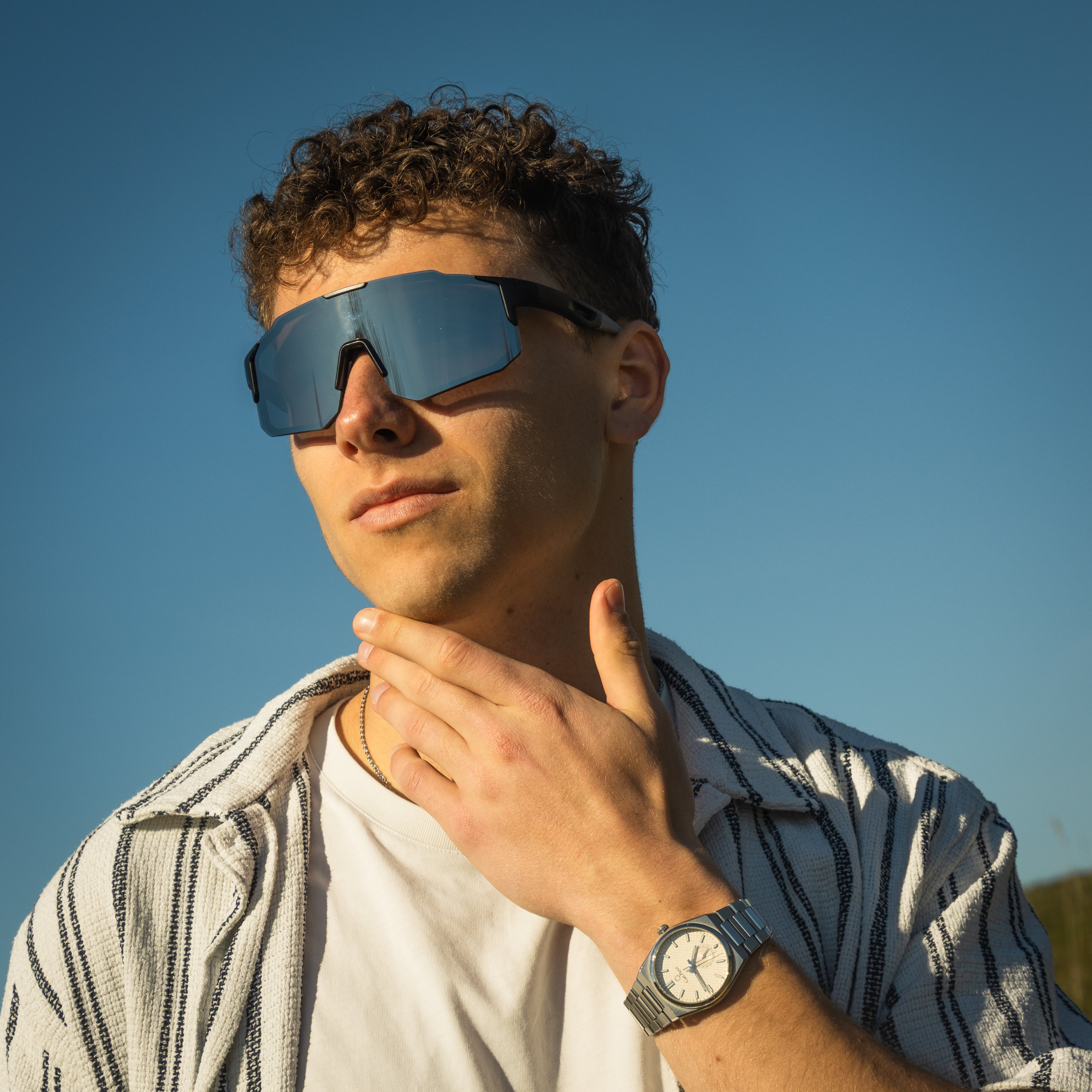 Mand med Noire Steely sportsbriller i grå med blå spejlglas mod blå himmel