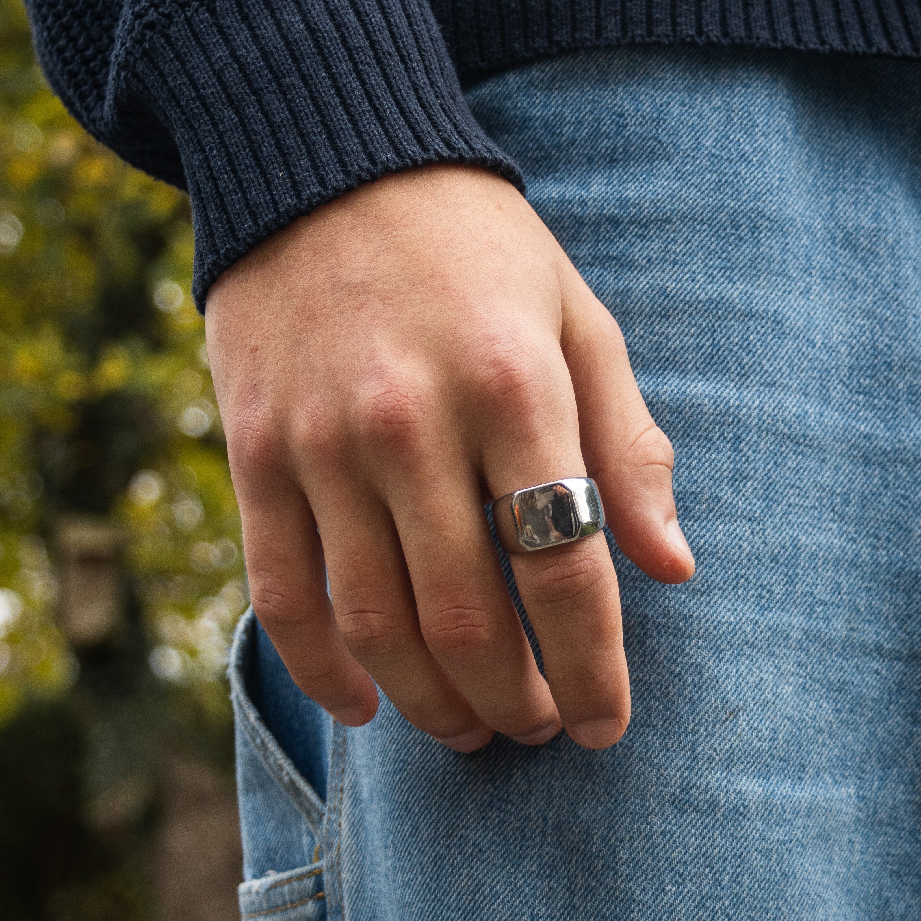 Sølvfarvet signetring på finger med blå sweater og jeans