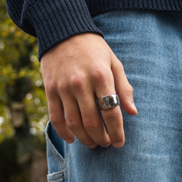 Sølvfarvet signetring på finger med blå sweater og jeans