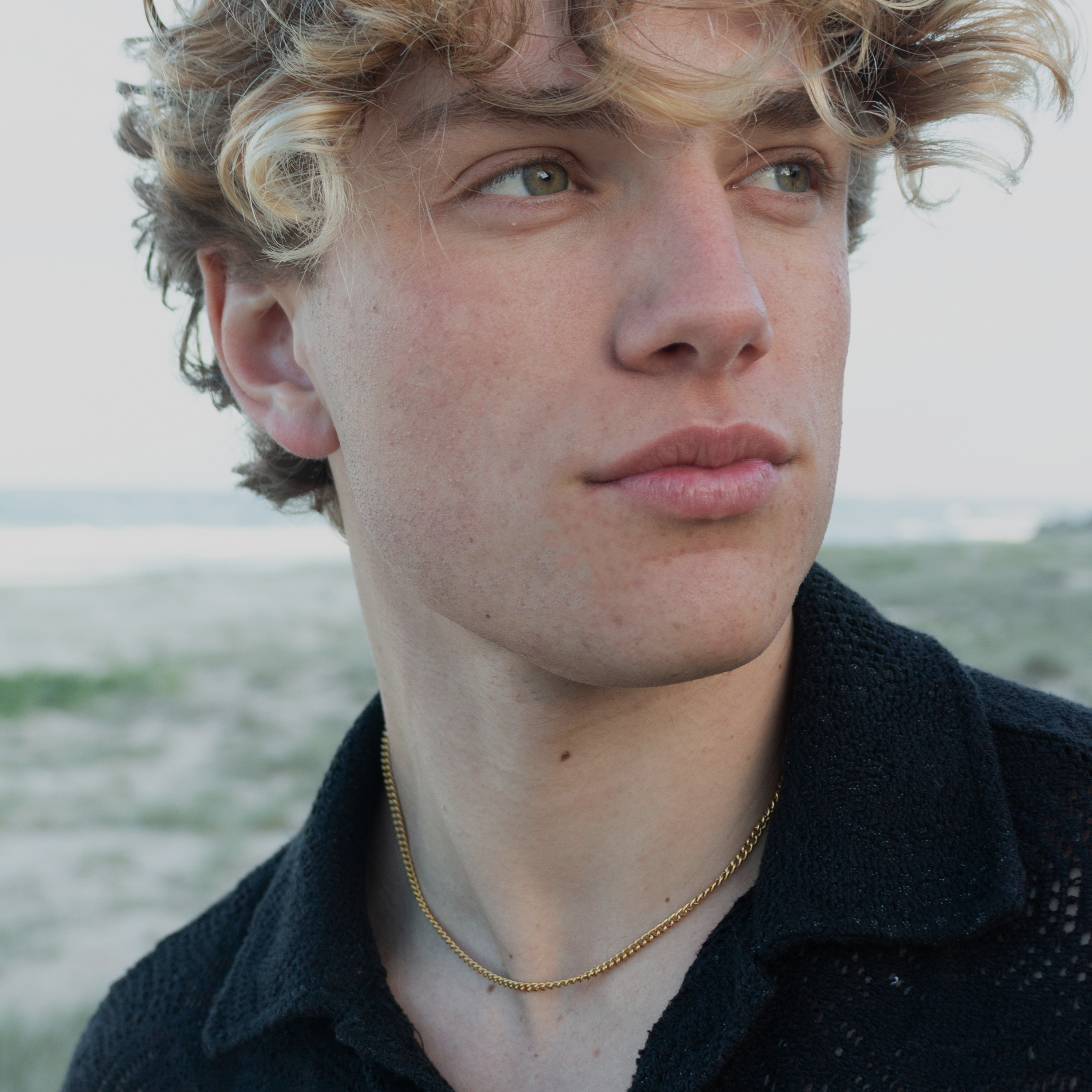 Ung mand bærer guldbelagt curb chain halskæde ved havet