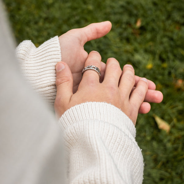 Sølvfarvet curb ring på finger med hvid sweater