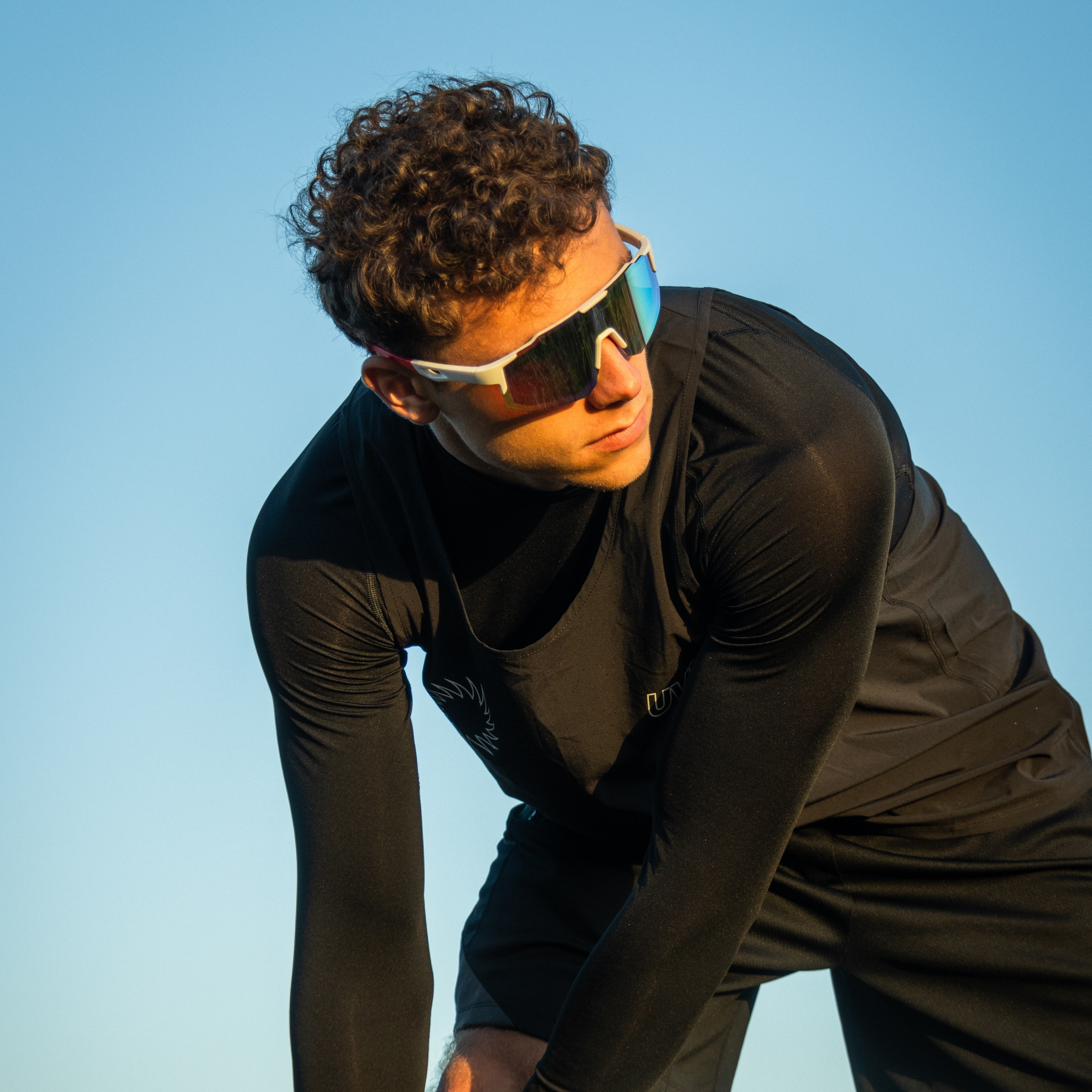 Mand i sort sportstøj bærer Noire Frost sportsbriller i hvid med blå spejlglas