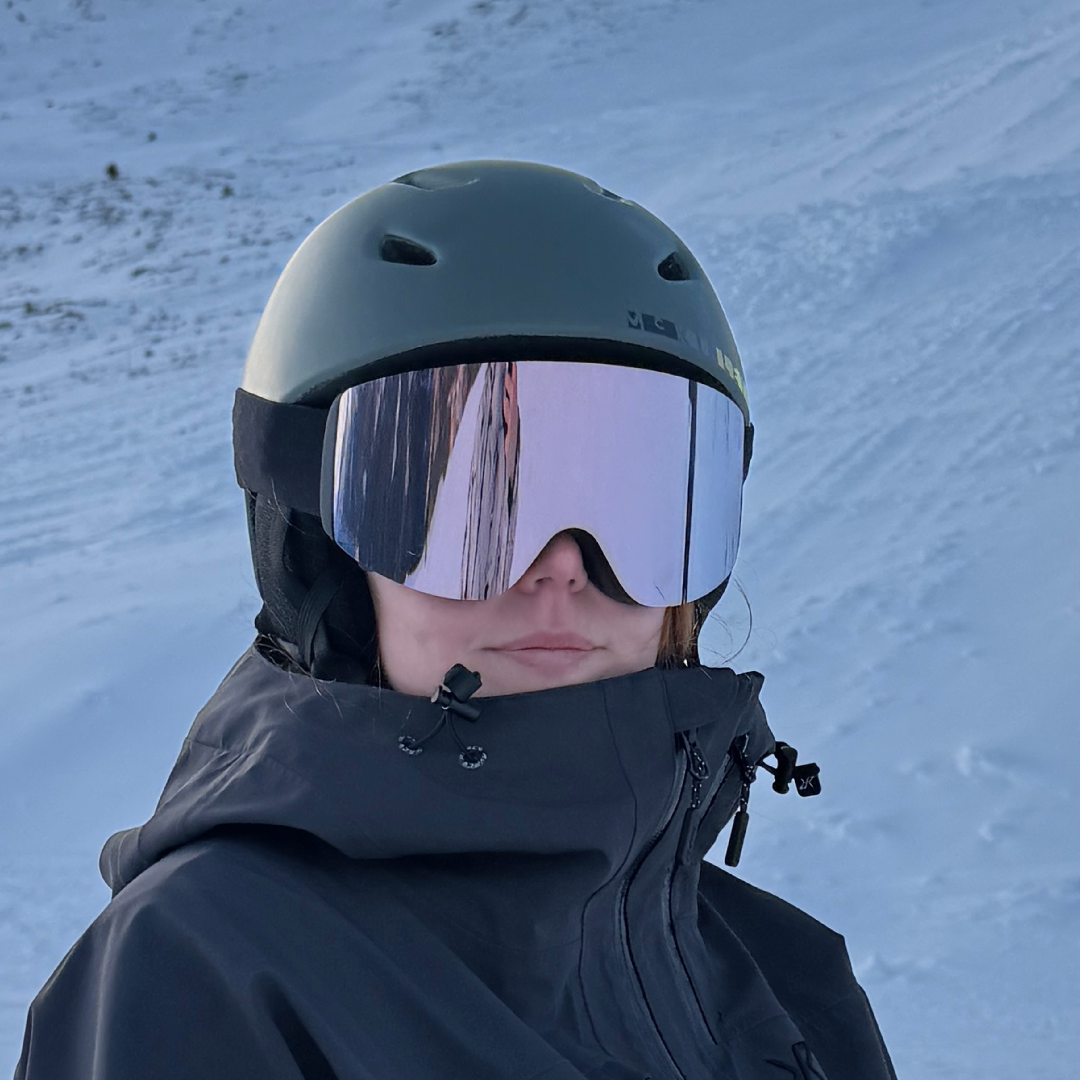 Skibriller med rosa spejlglas og hvid hjelm på snedækket piste