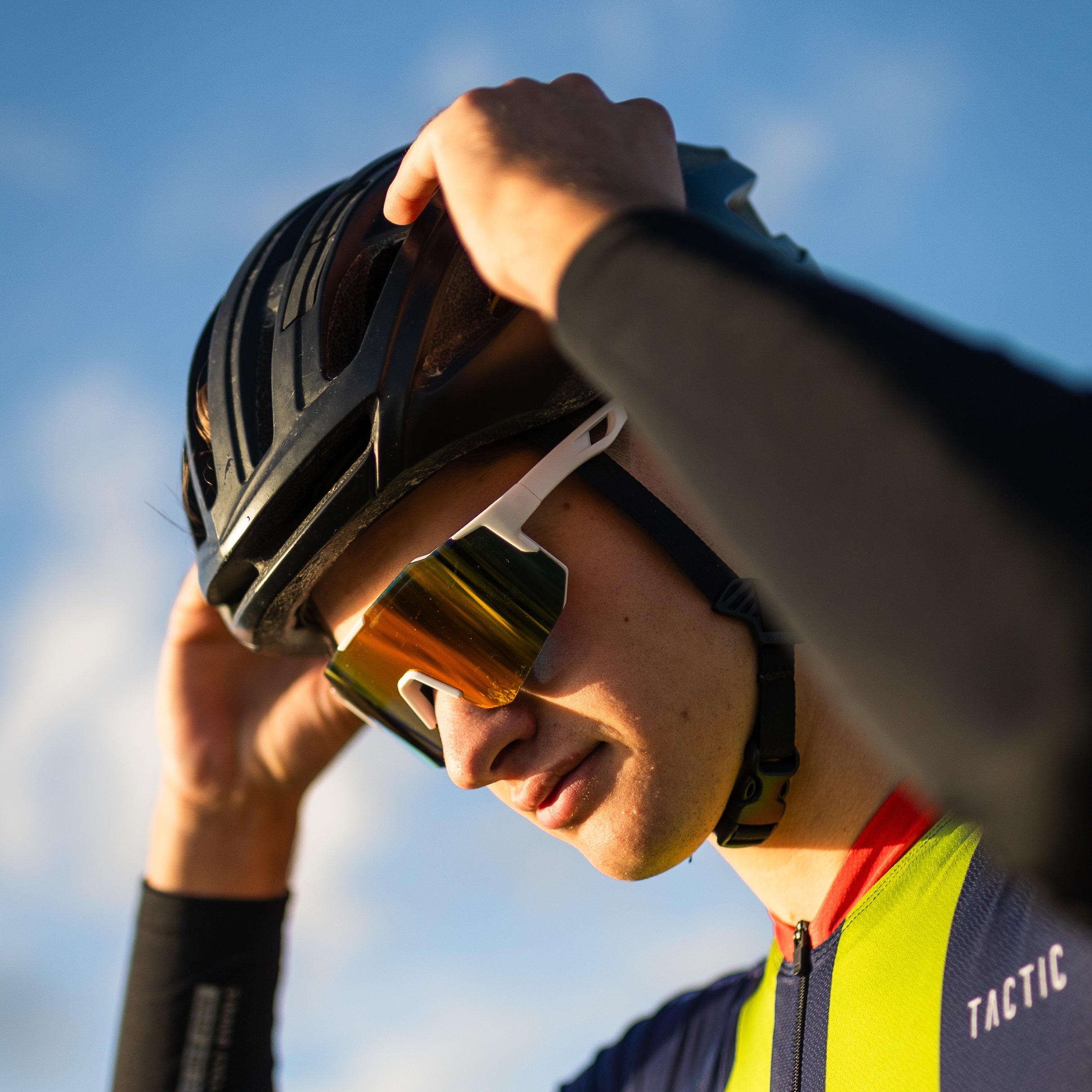 Cyklist med Noire Ruby sportsbriller i tropisk farve og sort cykelhjelm mod blå himmel