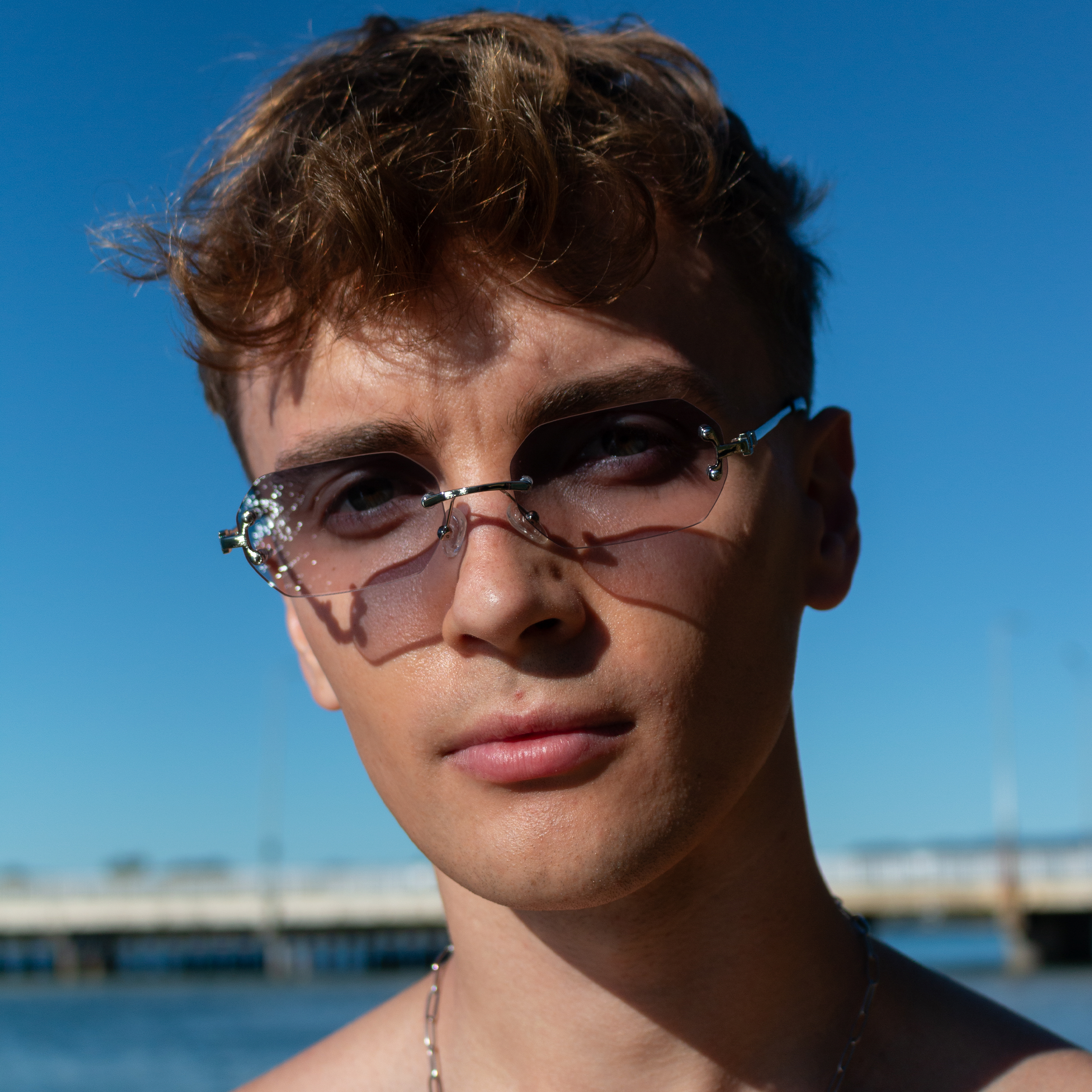 Young man with rimless sunglasses in gray shade against blue sky