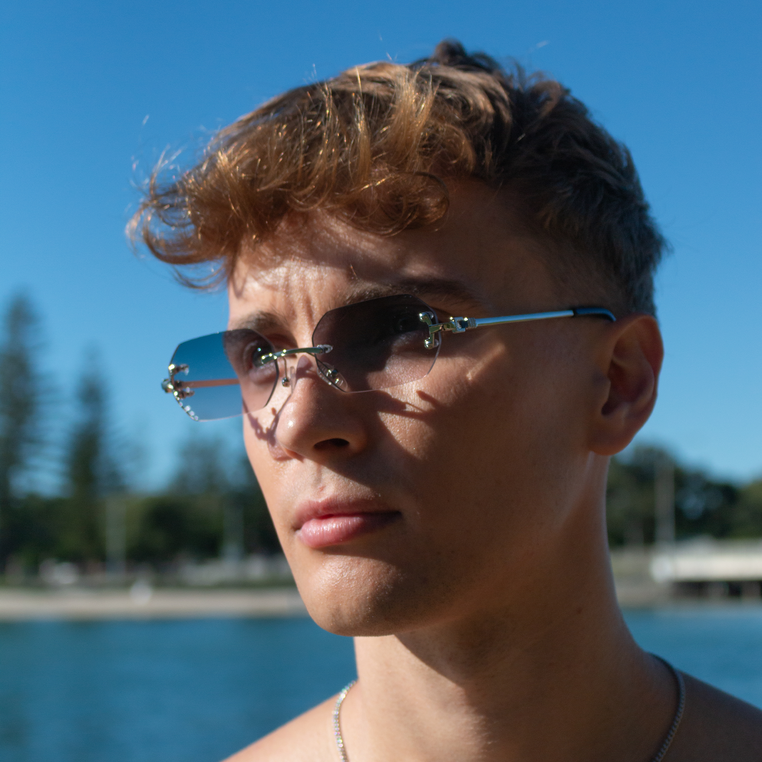 Young man with rimless sunglasses in shades of blue by the water