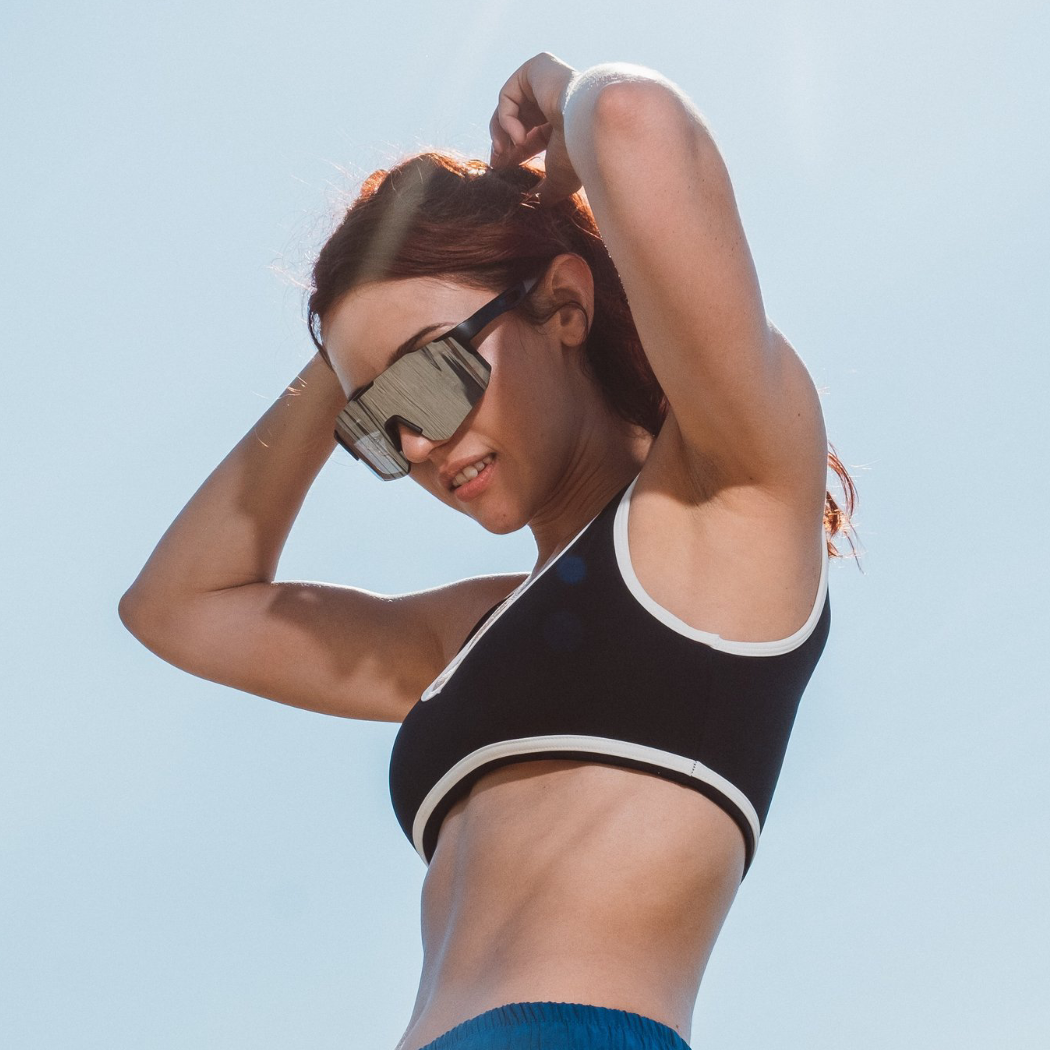 Kvinde bærer Noire Steely sportsbriller i grå under udendørs træning med blå himmel