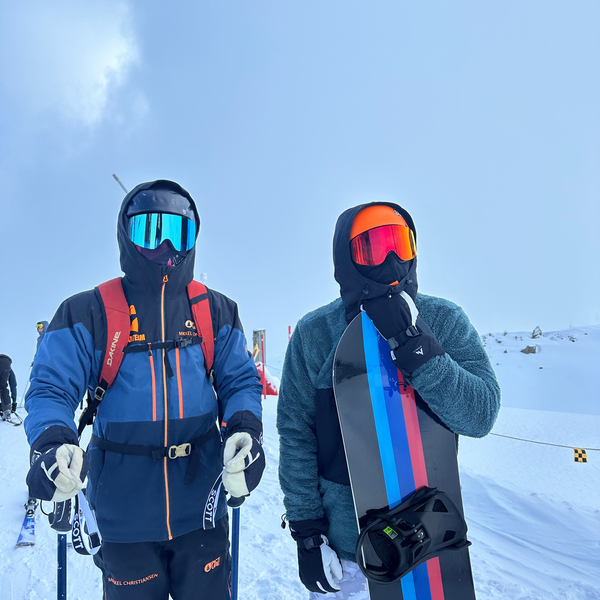 To skiløbere med Glaciér skibriller i blå og orange spejlglas på snedækket piste