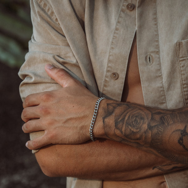Sølvfarvet panserkæde armbånd på tatoveret håndled med beige skjorte