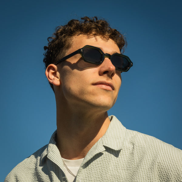 Mand bærer Noah Onyx solbriller i grøn mod blå himmel