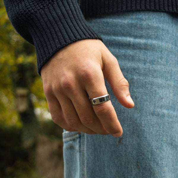 Sølvfarvet ring med kors-mønster på finger