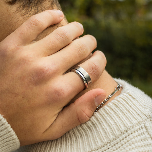 Sølvfarvet ring på finger med hvid strik i baggrunden