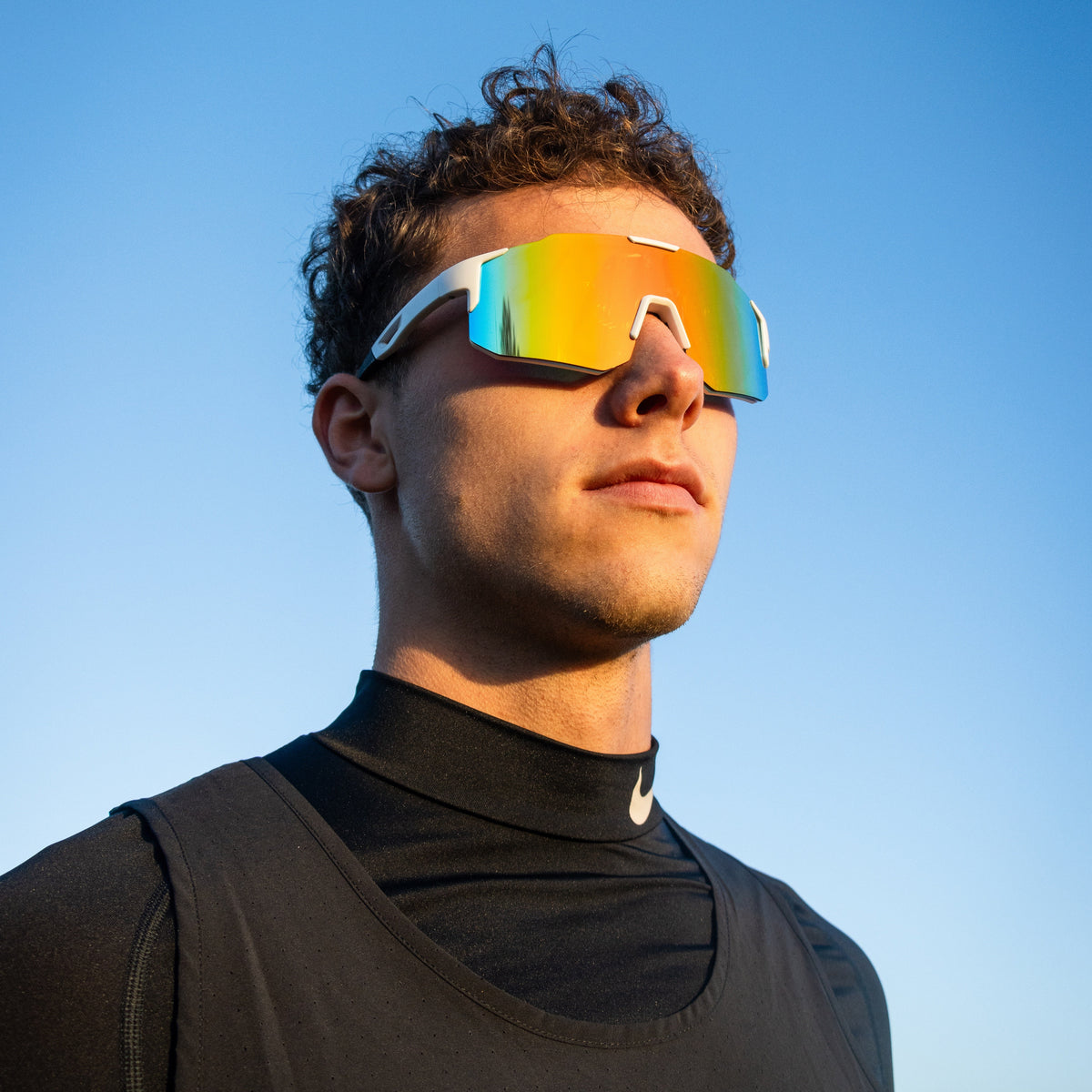 Sportsbriller med hvid stel og gul spejllinse på model mod blå himmel